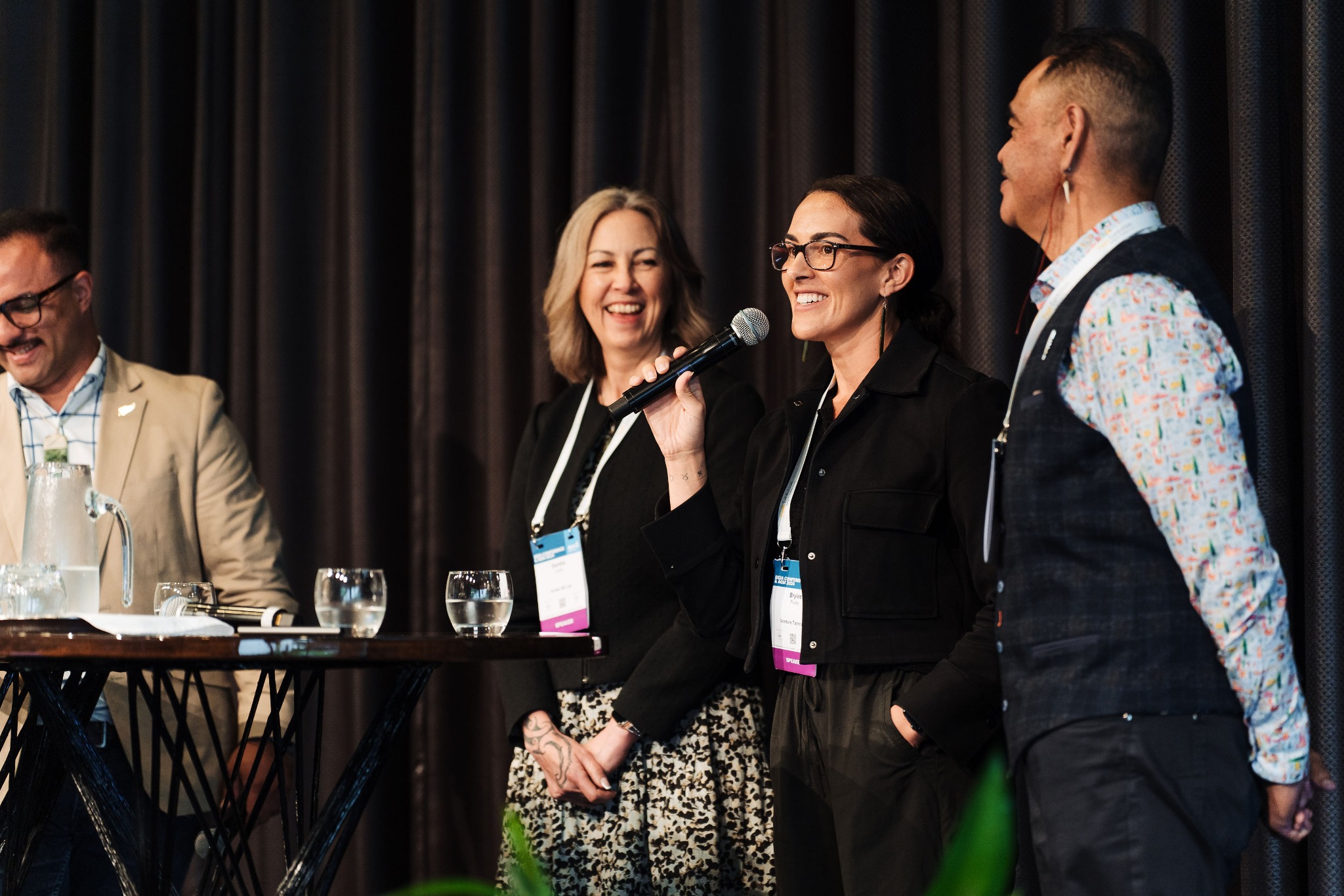 Brylee Flutey speaking into a microphone alongside fellow conference panellists